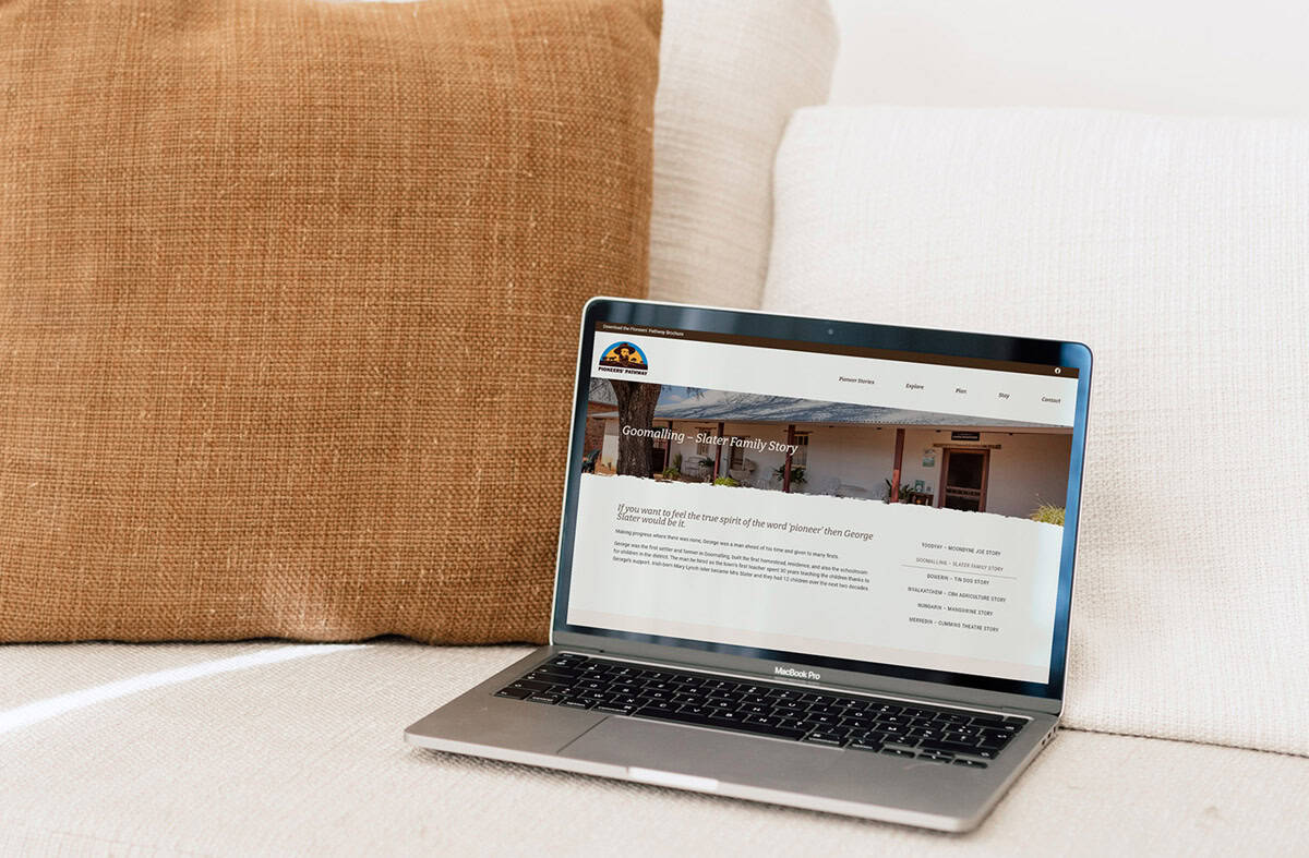 A laptop sits on a beige couch next to a brown pillow, displaying a tourism website design with text and a small banner image at the top.